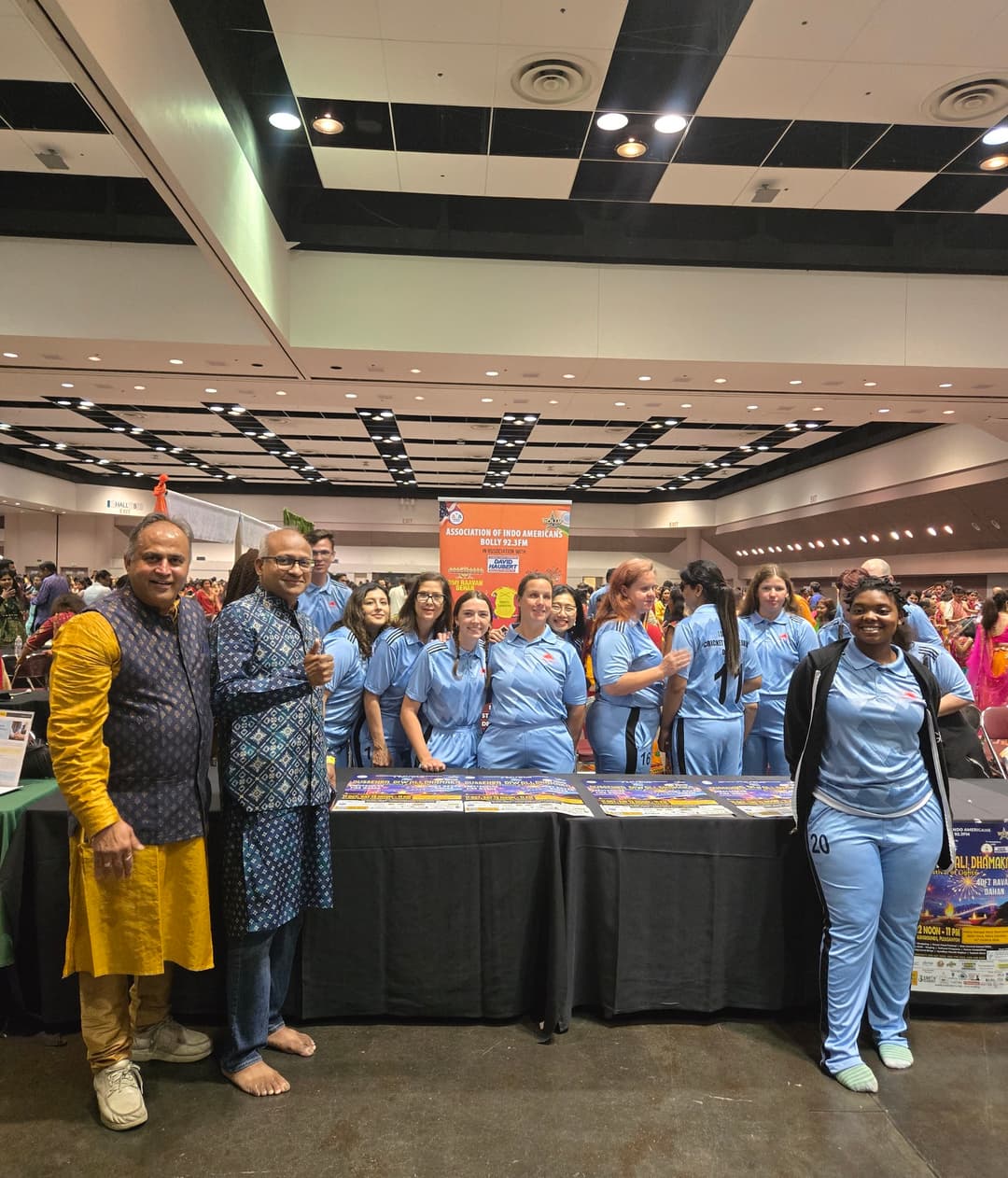 Some people are posing for the camera while some behind the table are busy chit-chatting.