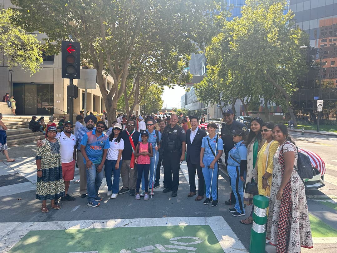 A group photo where few indian people are standing with a police officer and cricket team players.