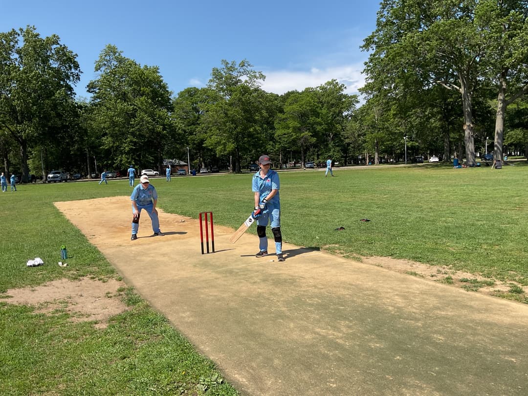 A bowler in the action to bowl, the ball has left her hand. The non striker, couple of fielders and the umpire are also visible in the shot. 