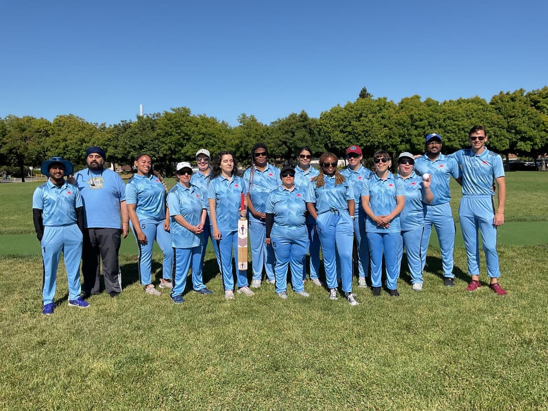 A bowler in the action to bowl, the ball has left her hand. The non striker, couple of fielders and the umpire are also visible in the shot. 