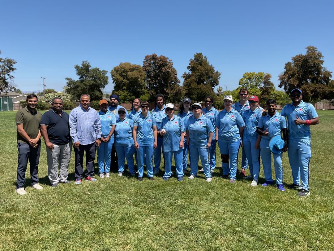 A bowler in the action to bowl, the ball has left her hand. The non striker, couple of fielders and the umpire are also visible in the shot. 
