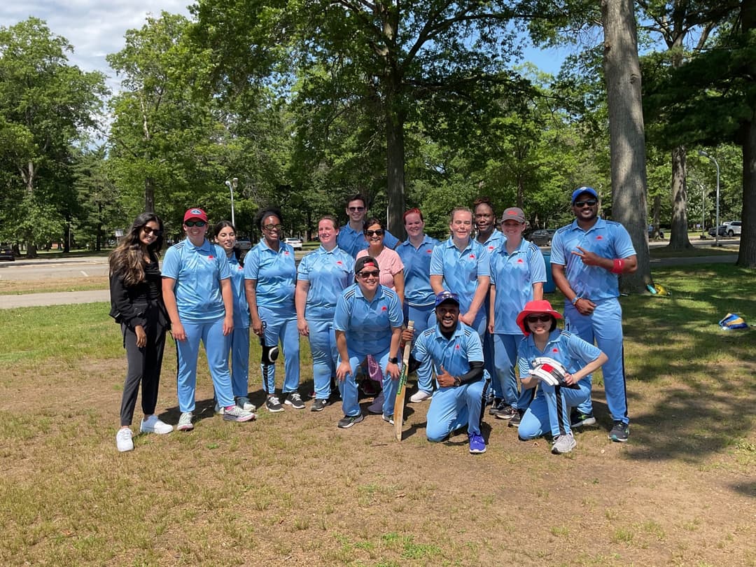 A bowler in the action to bowl, the ball has left her hand. The non striker, couple of fielders and the umpire are also visible in the shot. 