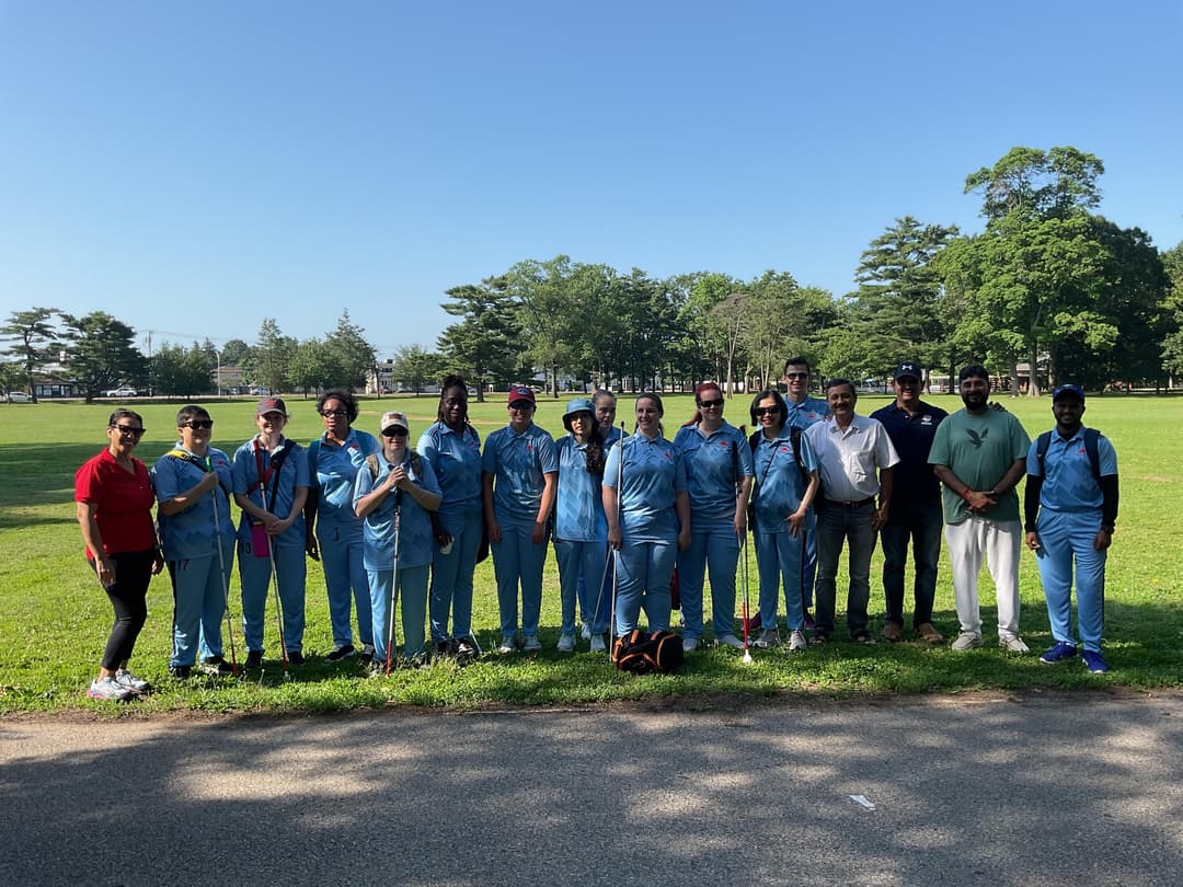 A bowler in the action to bowl, the ball has left her hand. The non striker, couple of fielders and the umpire are also visible in the shot. 