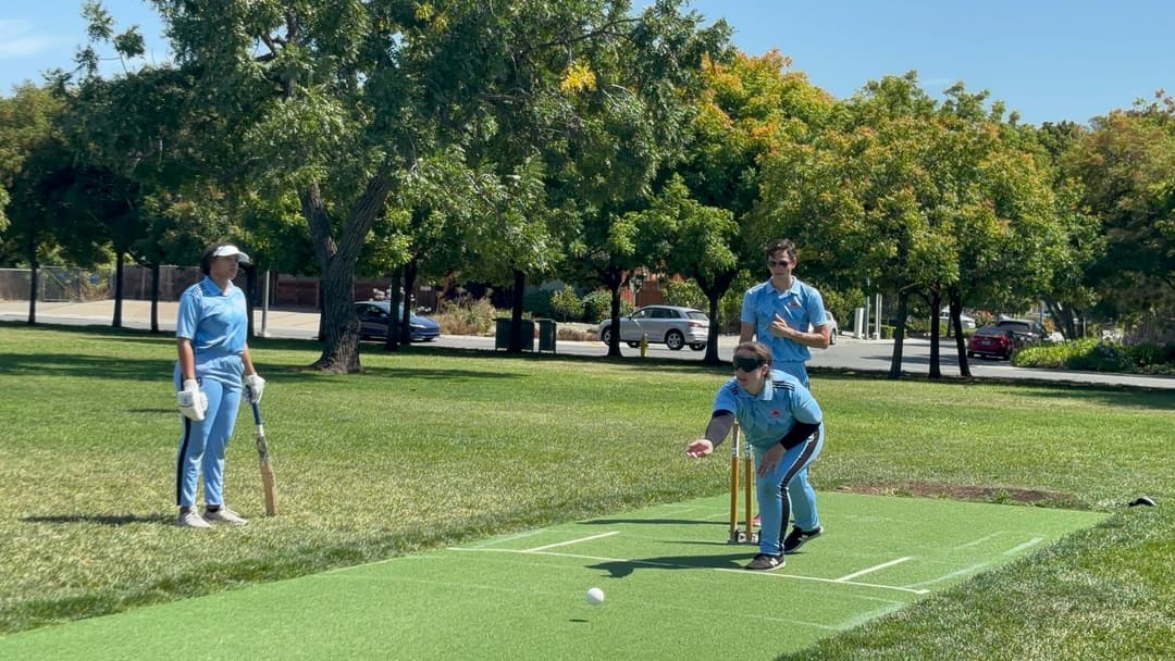 A bowler in the action to bowl, the ball has left her hand. The non striker, couple of fielders and the umpire are also visible in the shot. 