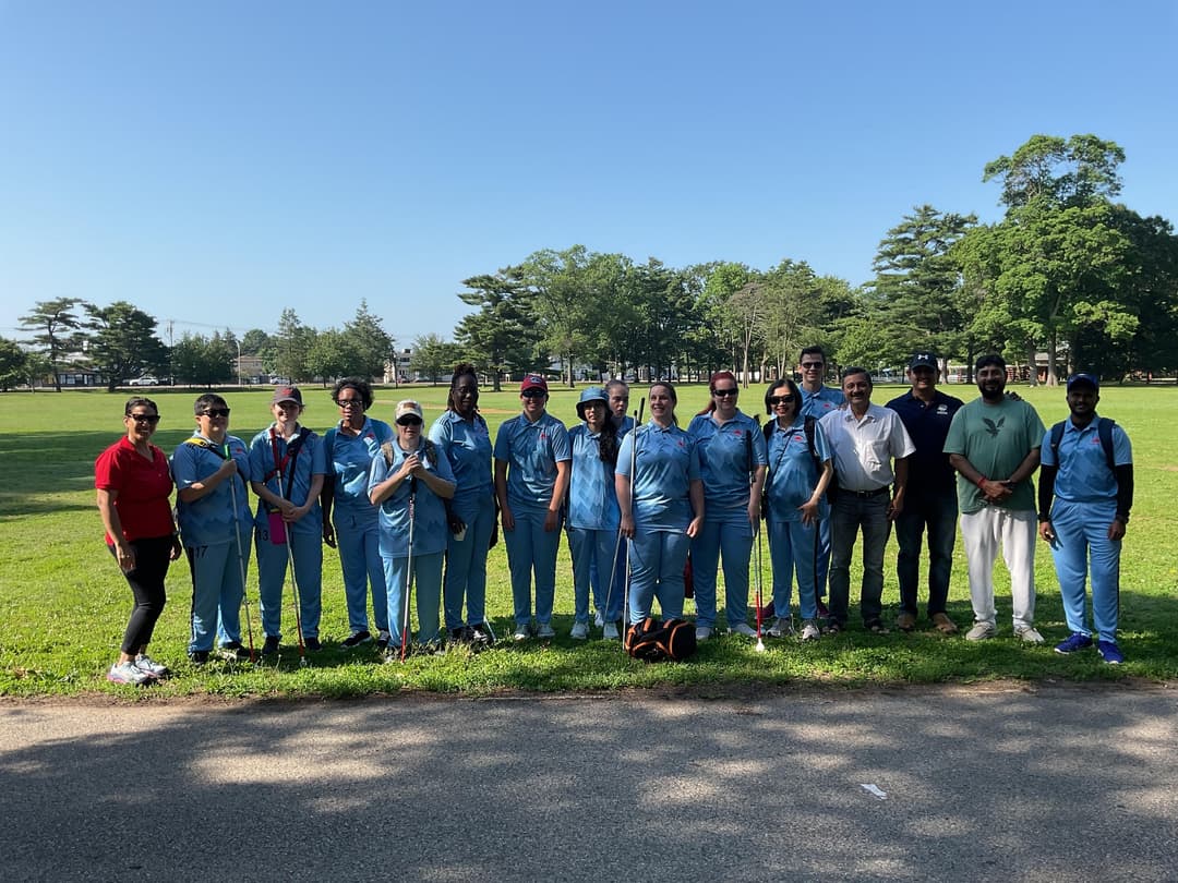A bowler in the action to bowl, the ball has left her hand. The non striker, couple of fielders and the umpire are also visible in the shot. 