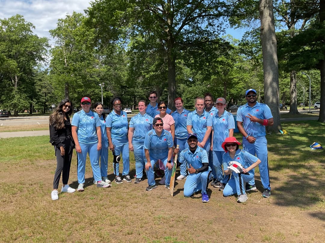 A bowler in the action to bowl, the ball has left her hand. The non striker, couple of fielders and the umpire are also visible in the shot. 