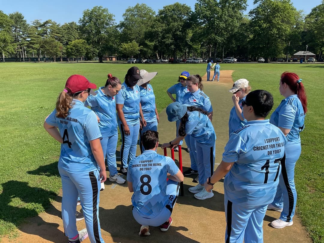A bowler in the action to bowl, the ball has left her hand. The non striker, couple of fielders and the umpire are also visible in the shot. 